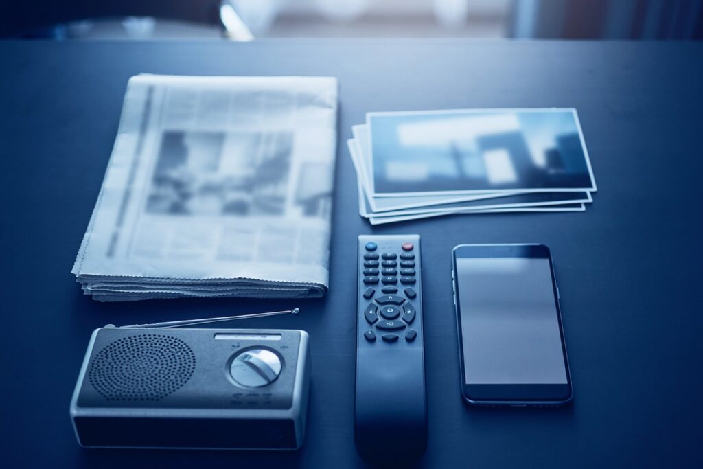 Newspaper, phone, remote, radio and billboard prints arranged on a desk